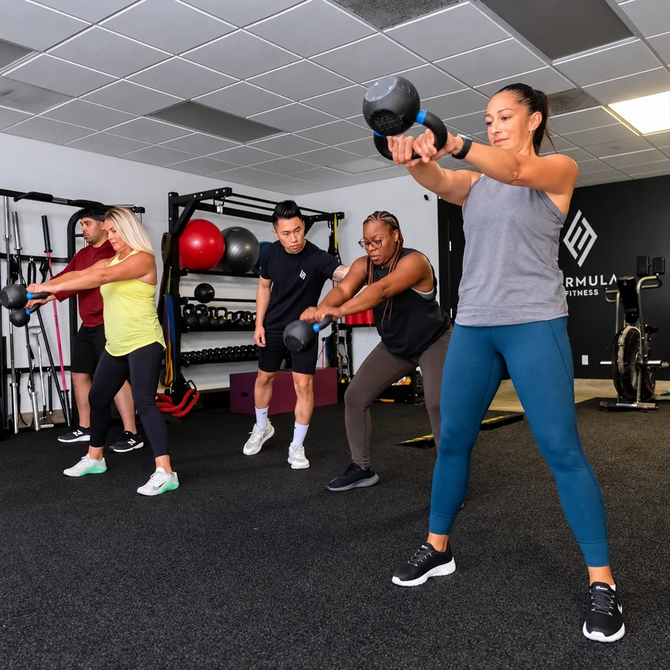 A Formula Fitness coach guiding a small group through a two-handed kettlebell swing