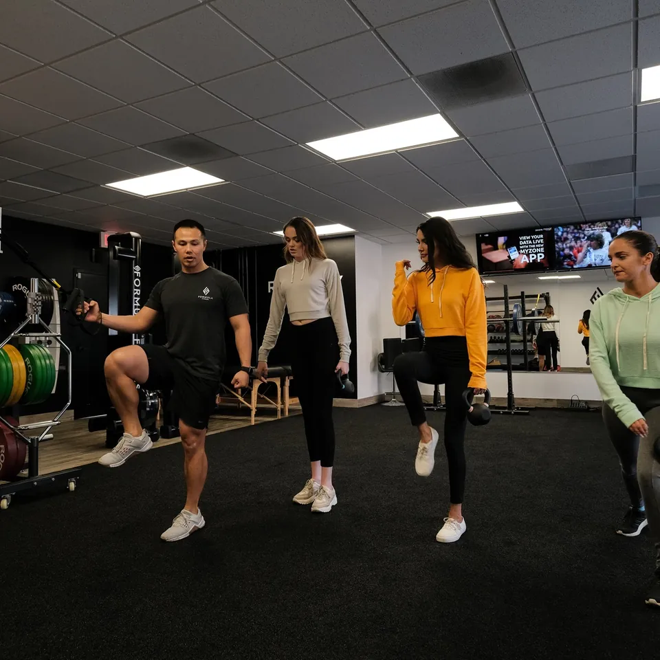 A Formula Fitness coach leading a small group through a standing knee raise while each person holds a kettlebell